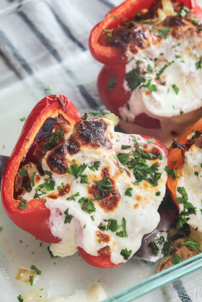 red bell pepper in a glass baking dish stuffed with philly cheesesteak mixture, melted cheese and baked
