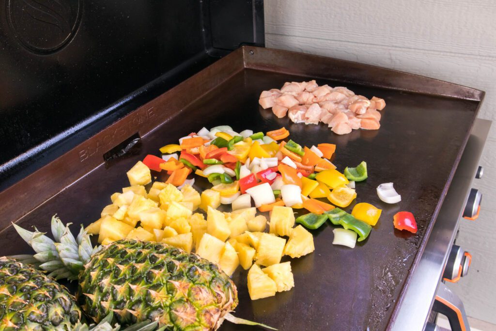 On the Blackstone: pineapple halves face down, pineapple chunks, veggie chunks and chicken