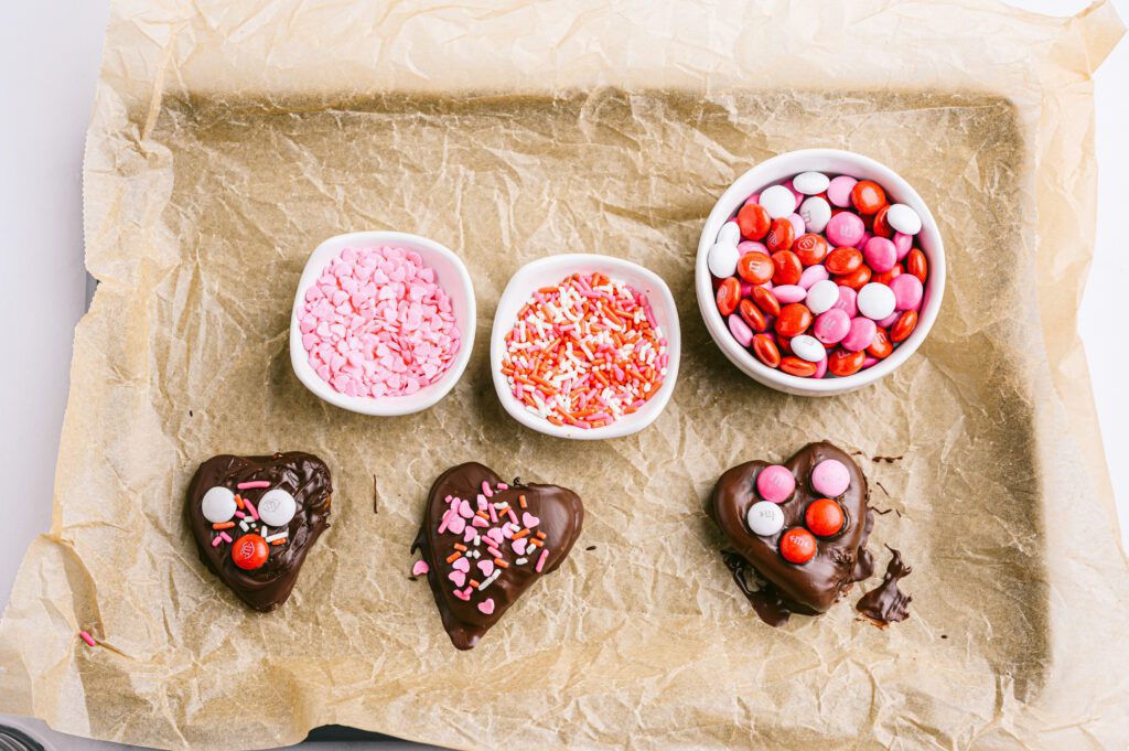 parchment paper on baking sheet with chocolate covered apple hearts, m&m's and sprinkles