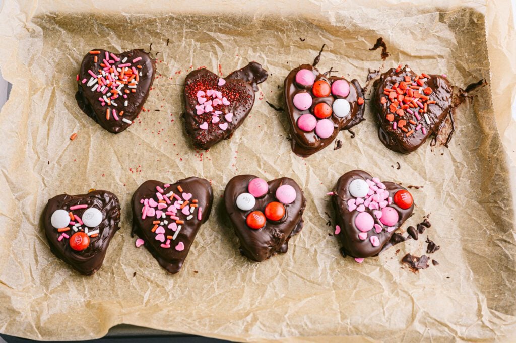 chocolate covered hearts on brown parchment paper on a baking sheet with sprinkles and M&m's