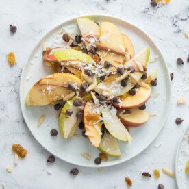 vertical shot of apple and pear nachos on a white plate with sliced almonds, golden raisins and chocolate chips