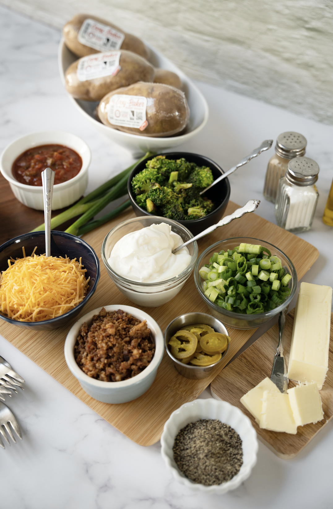 Baked potatoes in a bowl with toppings around it