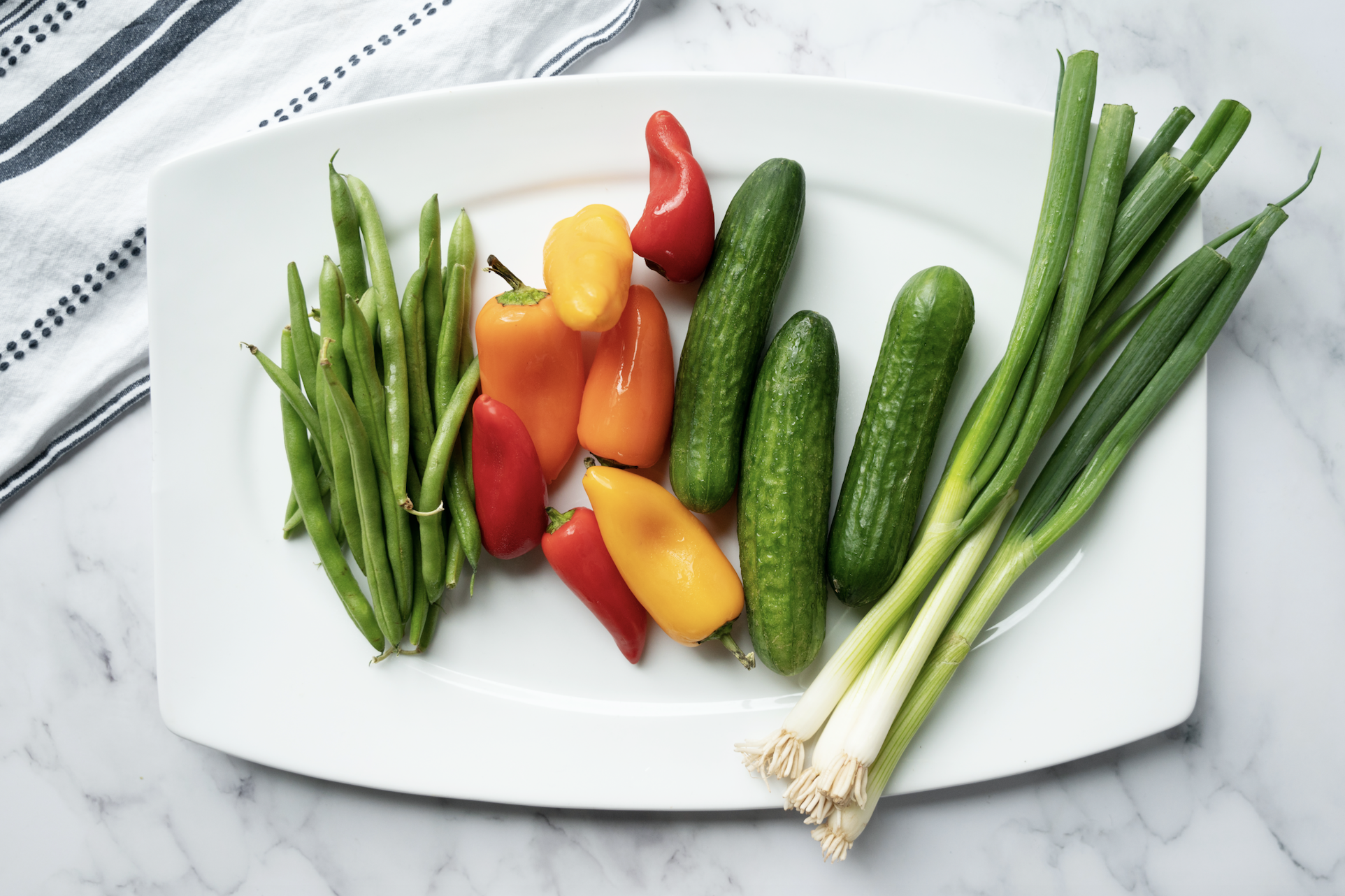 Plate of green beans, mini sweet peppers, mini seedless cucumbers and green onions