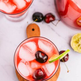 overhead shot of glass sitting on coaster with homemade cherry limeade recipe, ice, cherries and lime slice