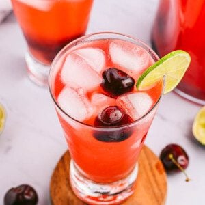 angled shot of homemade cherry limeade garnished with cherries, ice and lime slice