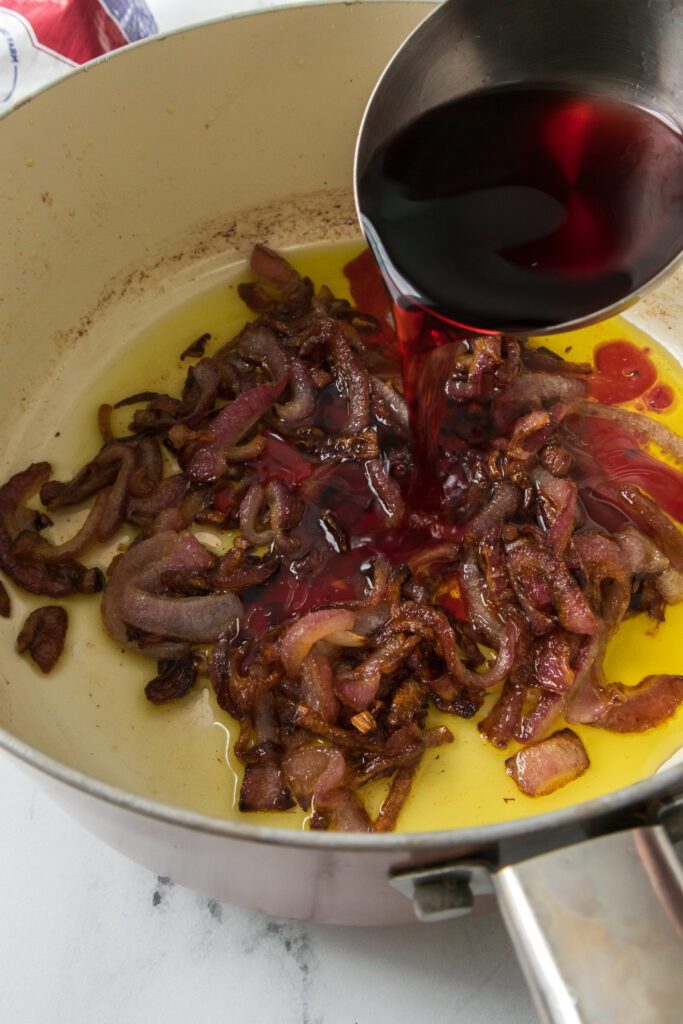 adding red wine to saucepan with onions