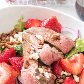 close up shot of steak and strawberry salad in white bowl