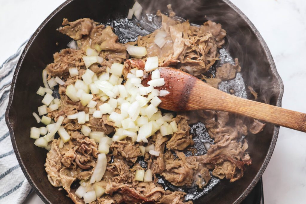 onions added to shaved steak in pan