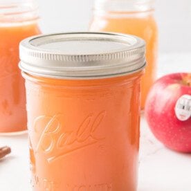 apple pie moonshine in mason jar with homemade apple cider and apple juice in background