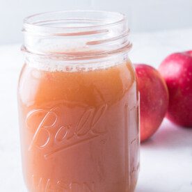vertical shot of homemade apple juice in mason jar with apples in background