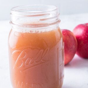 vertical shot of homemade apple juice in mason jar with apples in background
