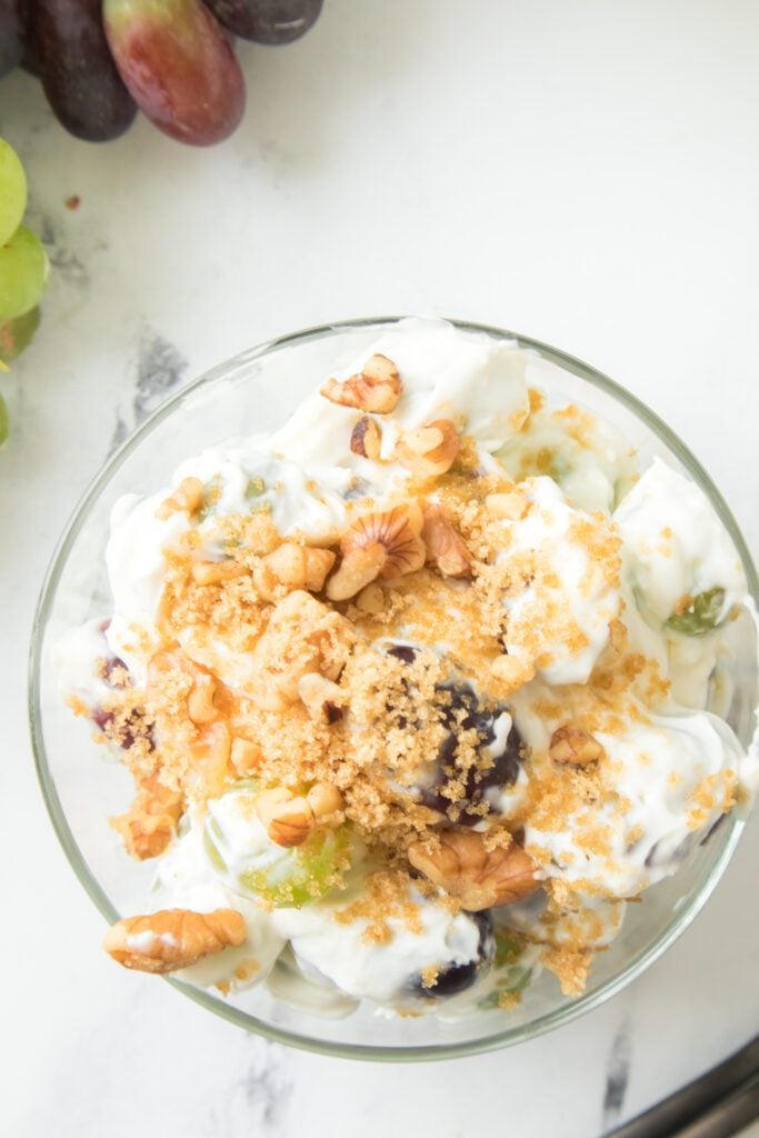 overhead shot of grape salad recipe in a glass bowl topped with brown sugar and walnuts