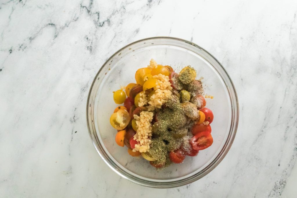 cherry tomatoes halved in glass bowl with olive oil, garlic, italian seasoning, salt and black pepper