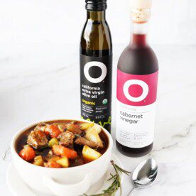 vertical image of beef stew in bowl with O Olive Oil & Vinegar bottles