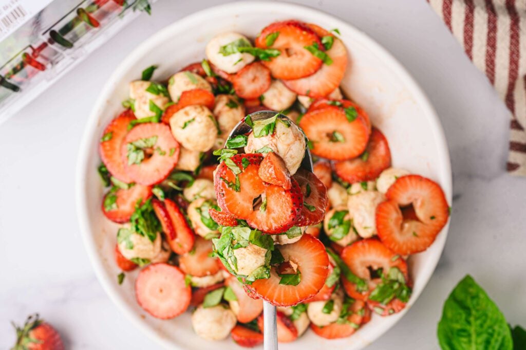 Fork holding a bite of the strawberry caprese salad over the bowl
