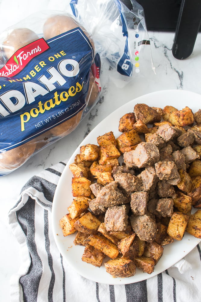 overhead shot of air fryer steak and potatoes on white plate with bag of wada farms idaho potatoes