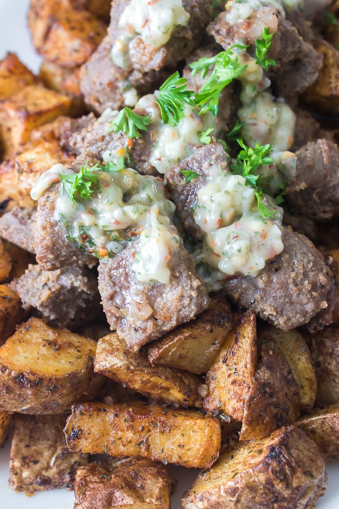 close up shot of garlic butter on top of steak and potatoes on the side