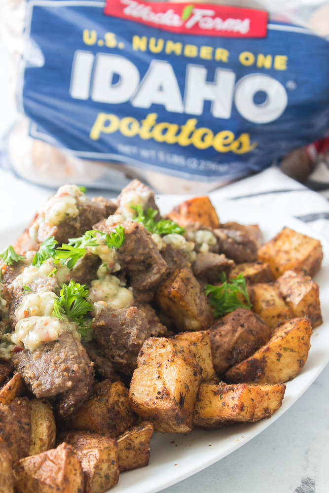 close up shot of steak and potato bites on a white plate with wada farms idaho potatoes in background