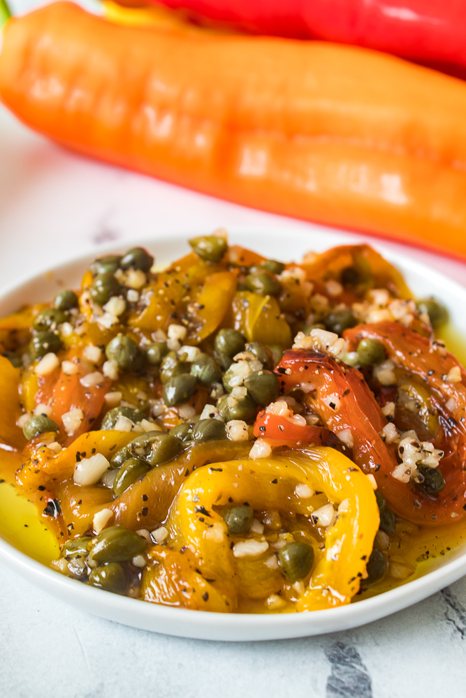 close up vertical shot of grilled peppers on white plate with capers and garlic