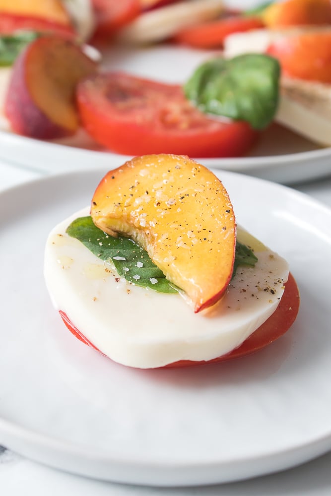 vertical close up shot of peach caprese, tomato, mozzarella, basil topped with a fresh peach