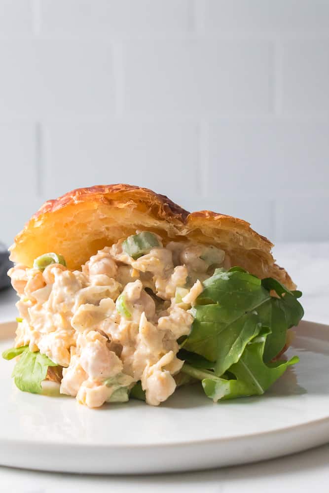 vertical close up shot of chickpea salad sandwich on a croissant with lettuce