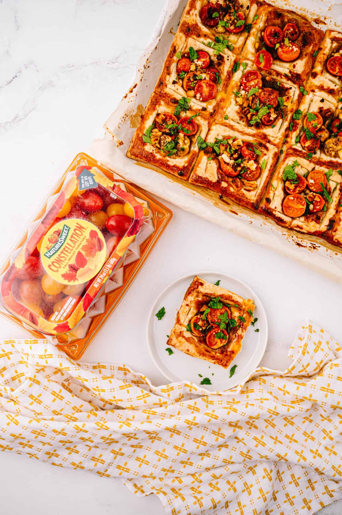 overhead shot of tomato tart on a small white plate with baking sheet of baked tarts