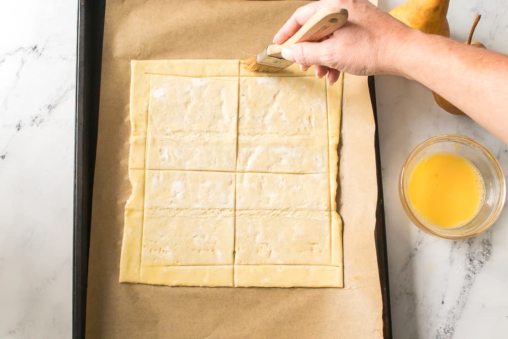 hand brushing egg wash on outside of puff pastry