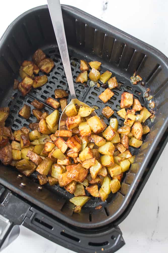 air fryer basket with serving spoon and potatoes that have been cooked