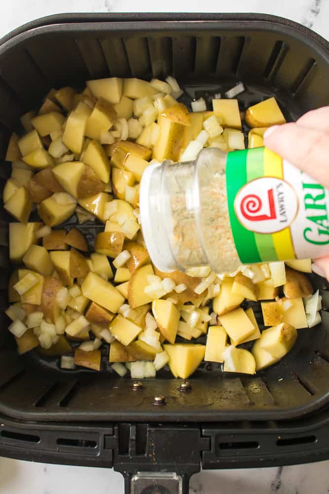 hand using garlic salt to sprinkle over chopped onions and potatoes