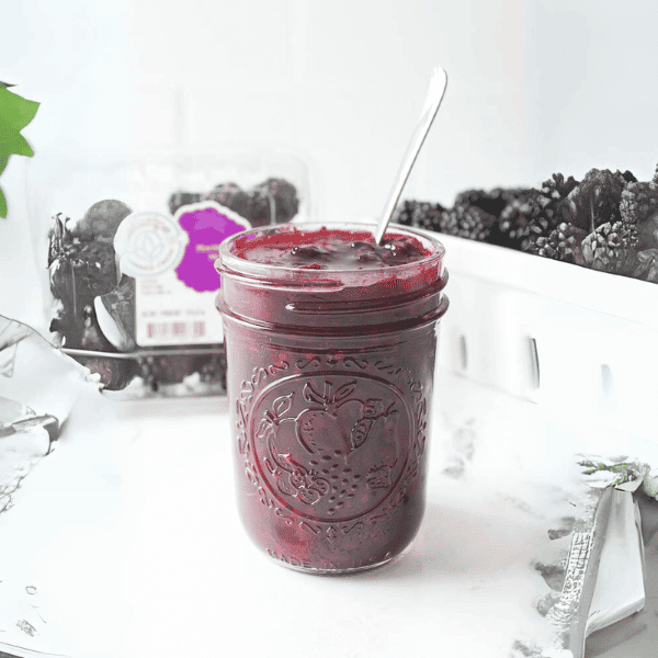 Homemade Blackberry Jam on kitchen counter with blackberries in background