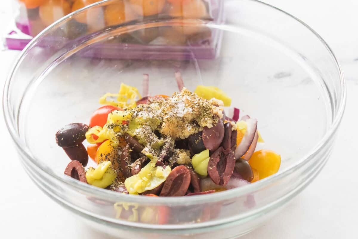 red onion, cherry tomatoes, black olives, olive oil, oregano and salt and pepper in glass bowl