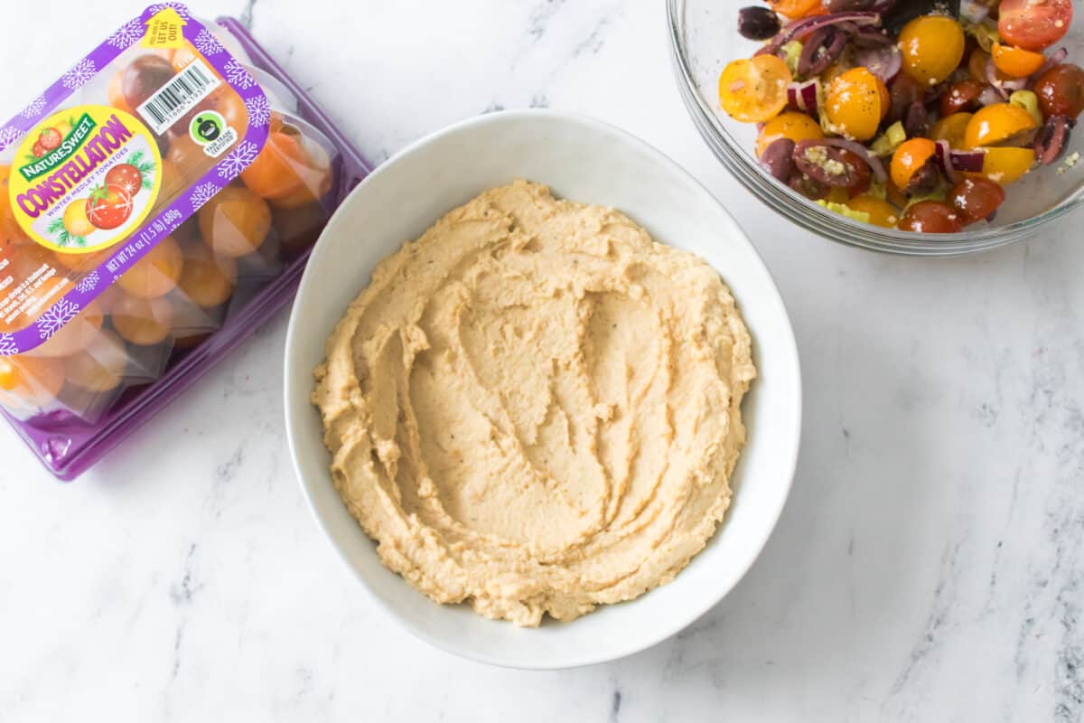 hummus in white bowl with cherry tomatoes mixed in glass bowl