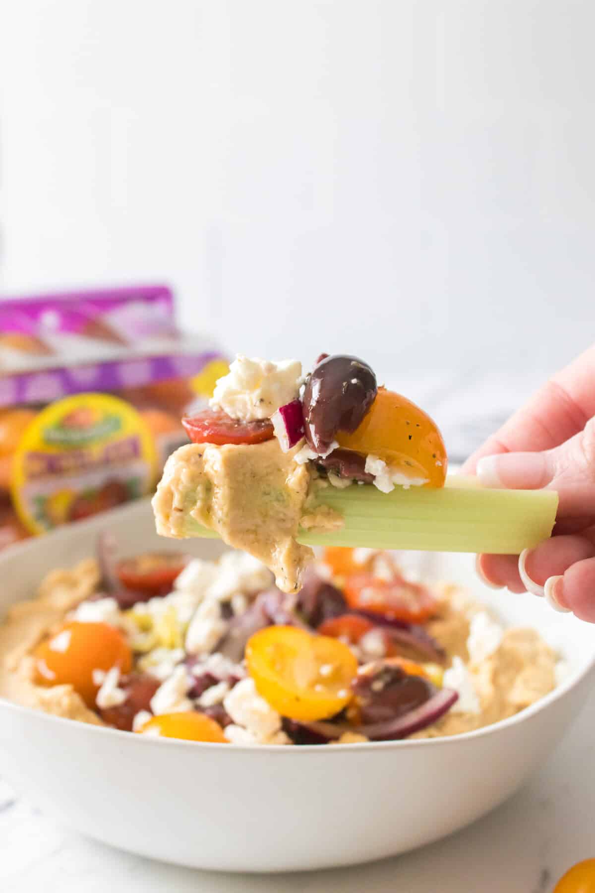 celery holding a bite of loaded greek hummus