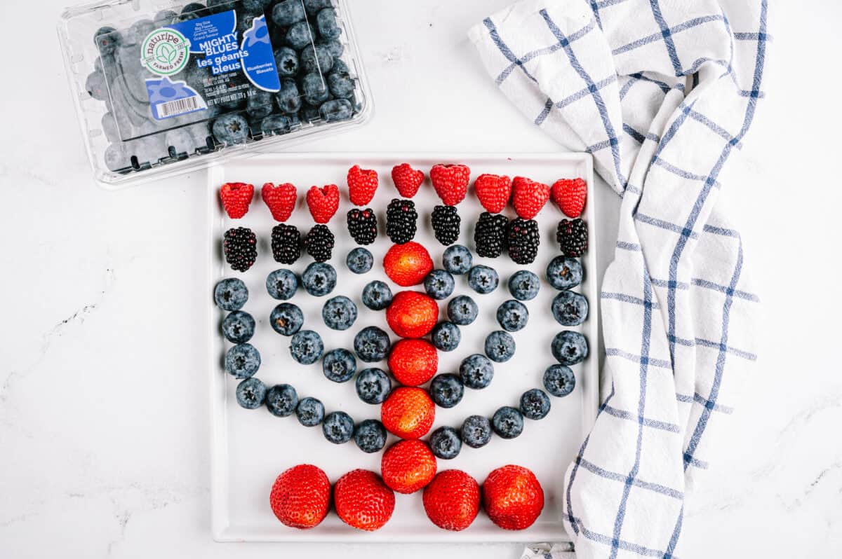 overhead shot of strawberries, blueberries, blackberries and raspberries on a plate shaped like a menorah