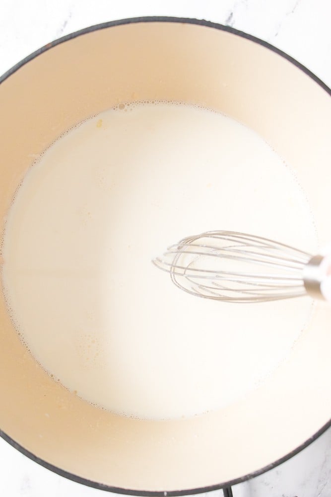 milk added to dutch oven with melted butter and flour being whisked