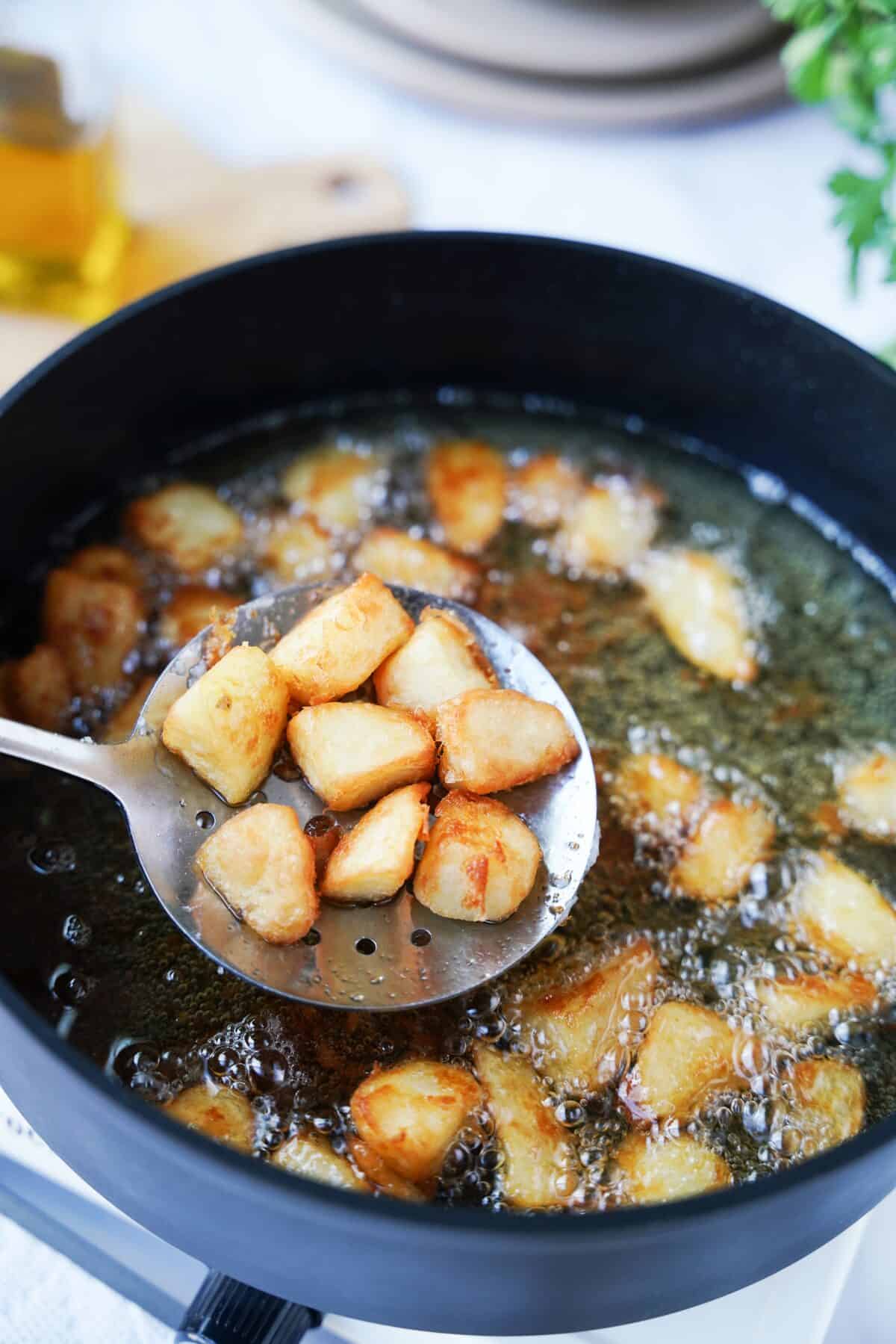 removing fried potatoes from skillet with slotted spoon