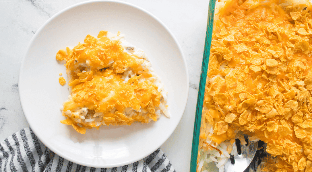 Funeral potatoes on a white plate next to glass dish serving funeral potatoes