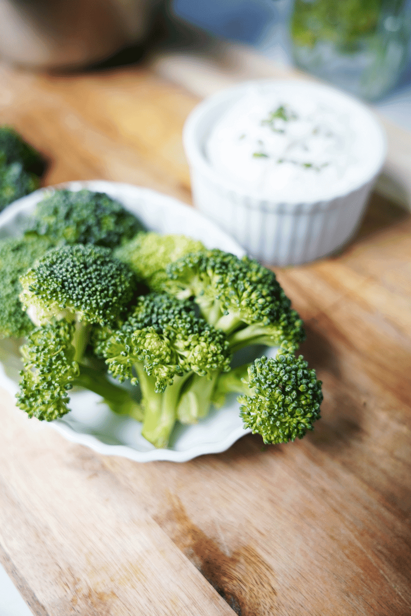 Broccoli on a cutting board with dressing in background
