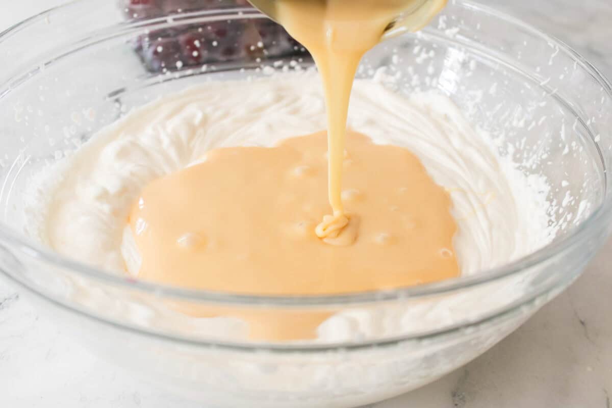 sweetened condensed milk being poured into heavy whipping cream that has been beaten