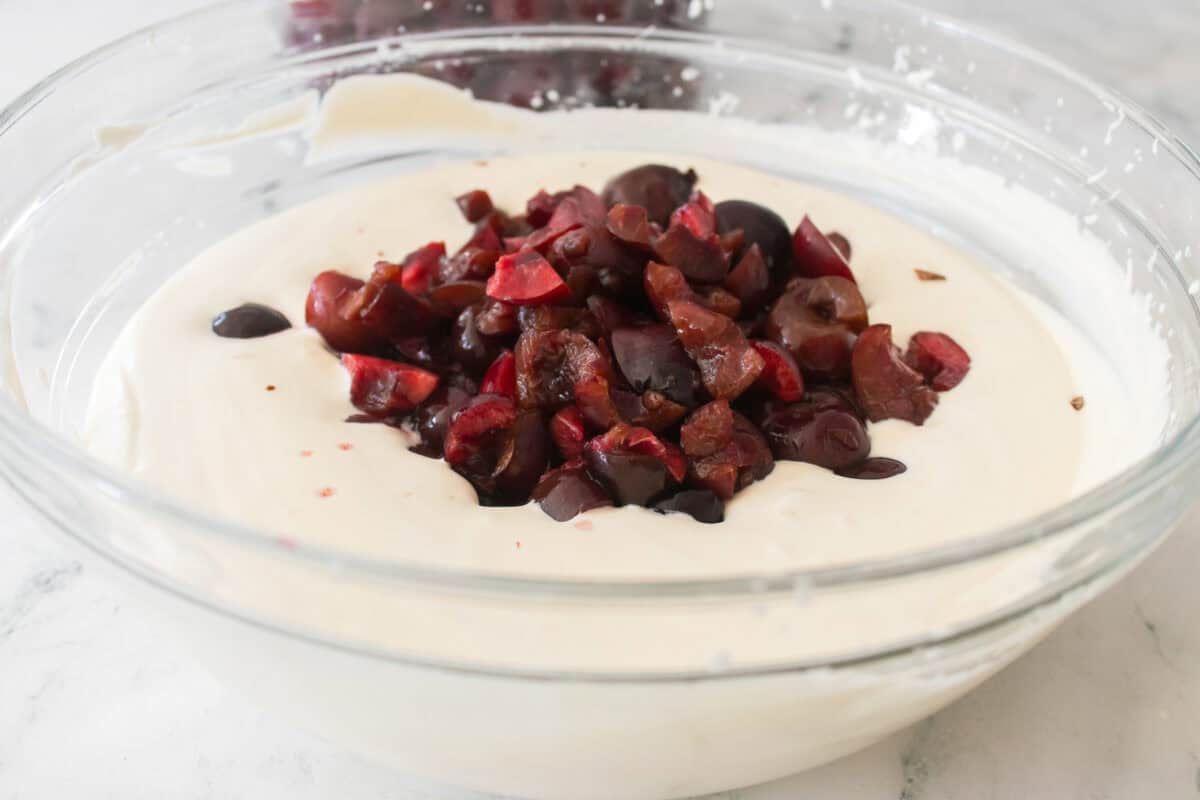 chocolate chunks and cherries added to glass bowl of heavy whipping cream and sweetened condensed milk
