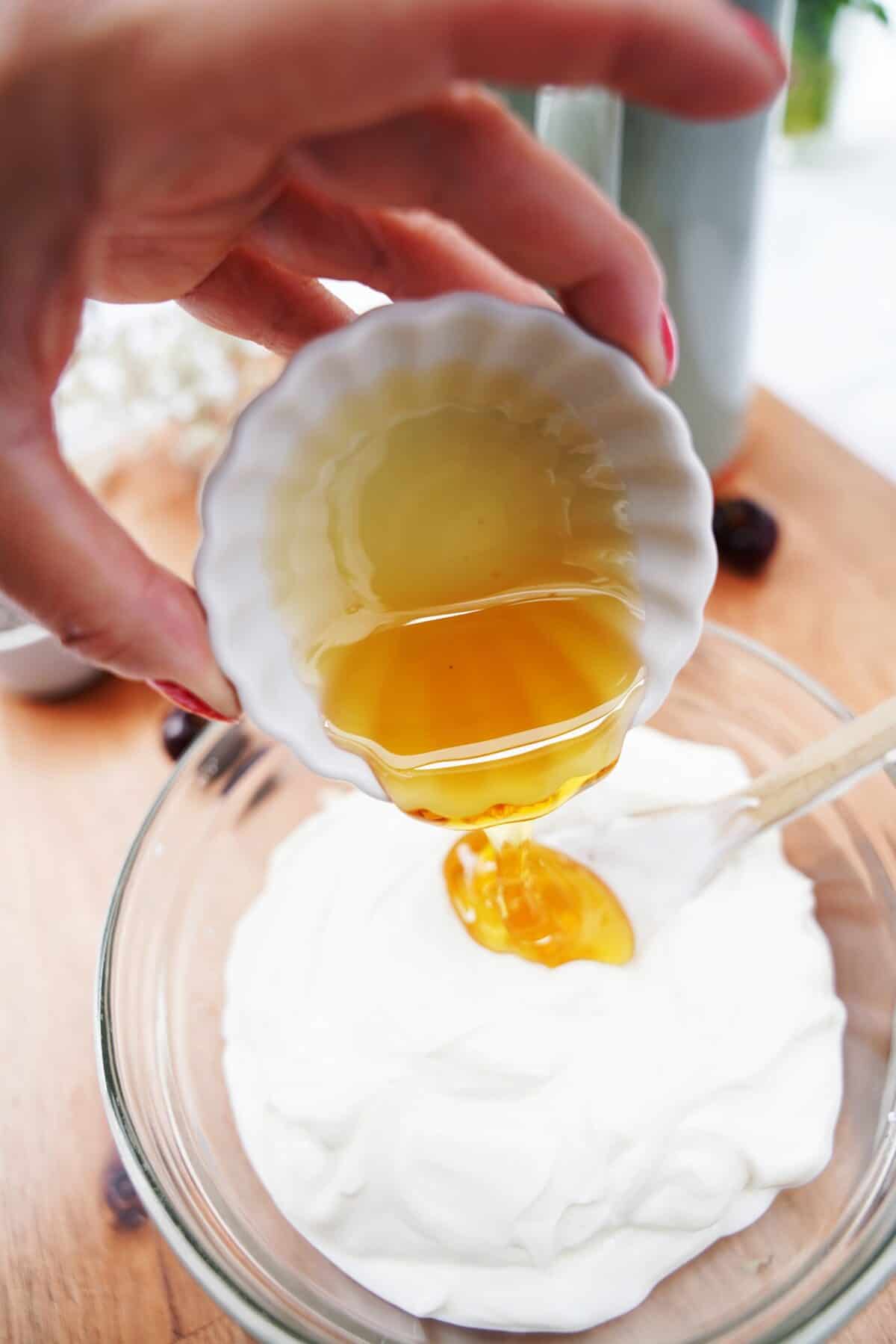 honey being poured into a bowl of plain Greek yogurt