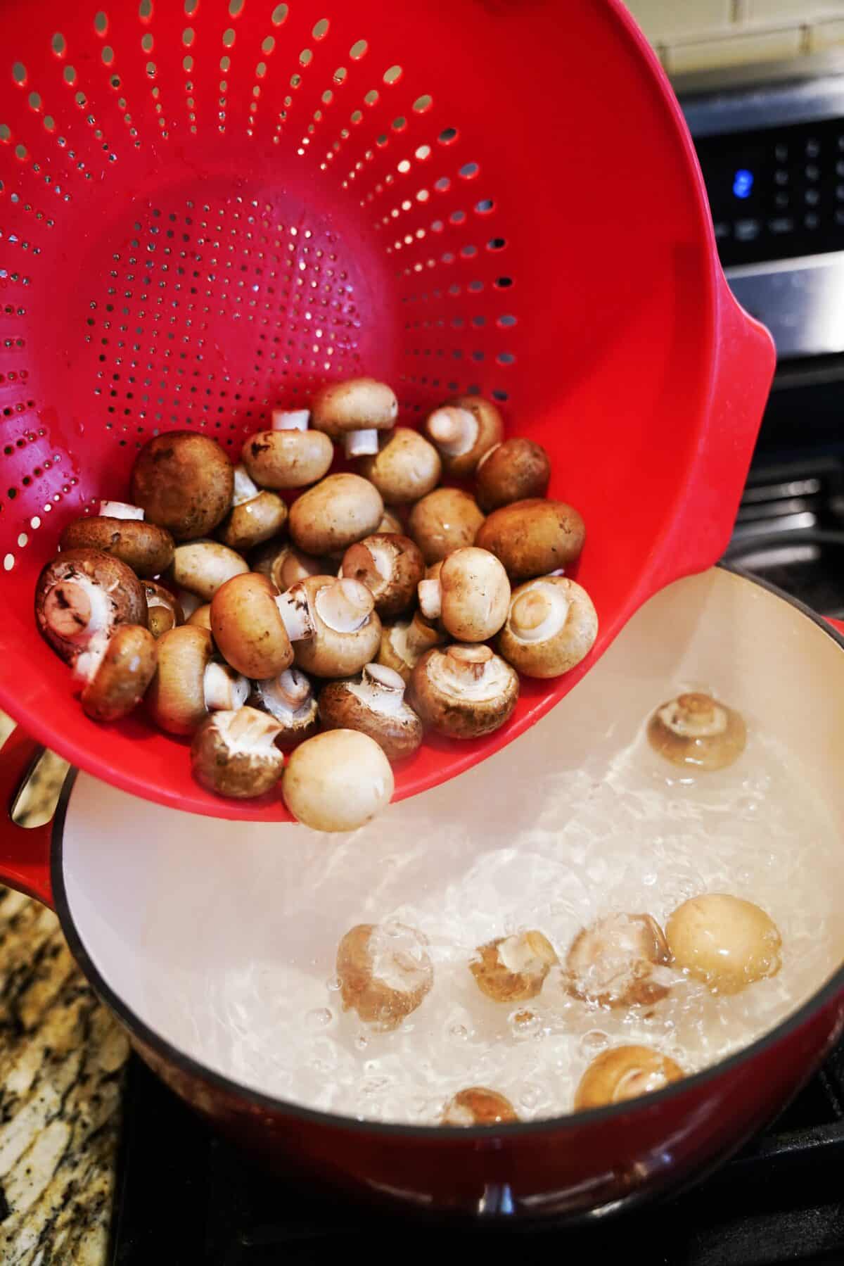 strainer pouring clean mushrooms into pot of boiling water