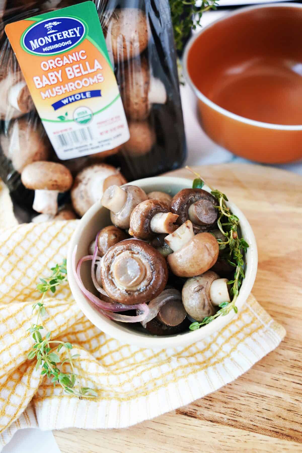 pickled mushrooms in bowl on cutting board with fresh thyme