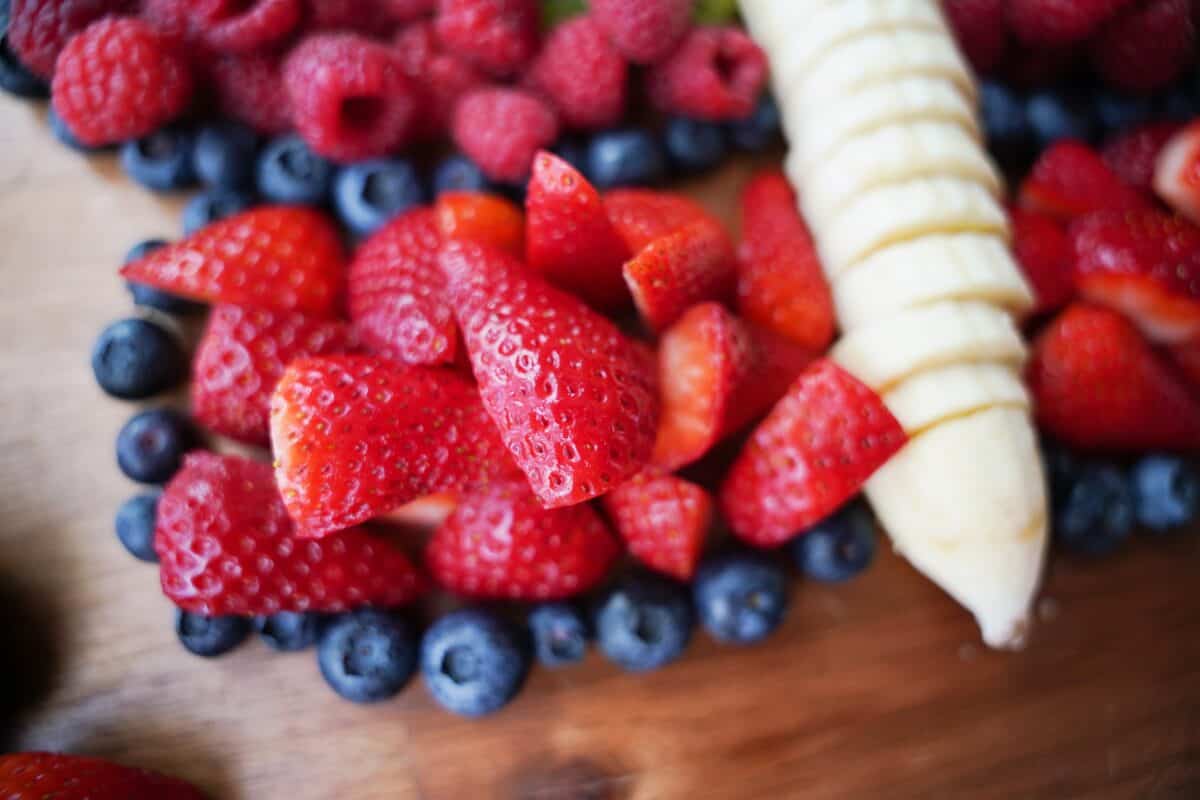 close up shot of quartered strawberries surrounded by blueberries and banana slices
