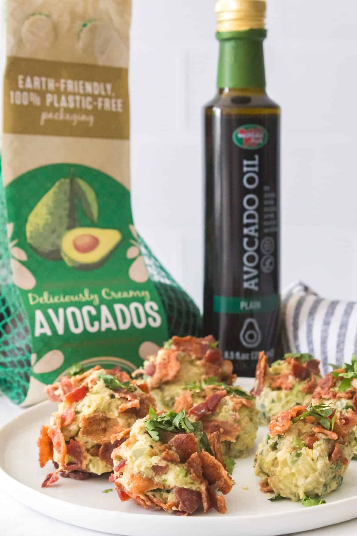 8 bacon guacamole fat bombs on white plate with bag of avocados and avocado oil in background