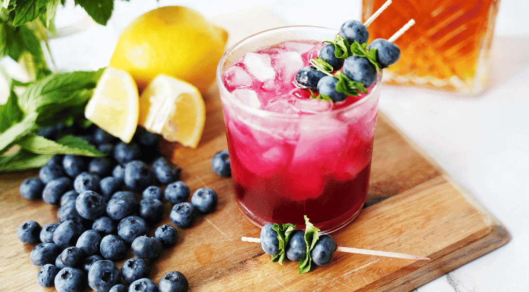 Blueberry Bourbon Smash in glass surrounded by blueberries