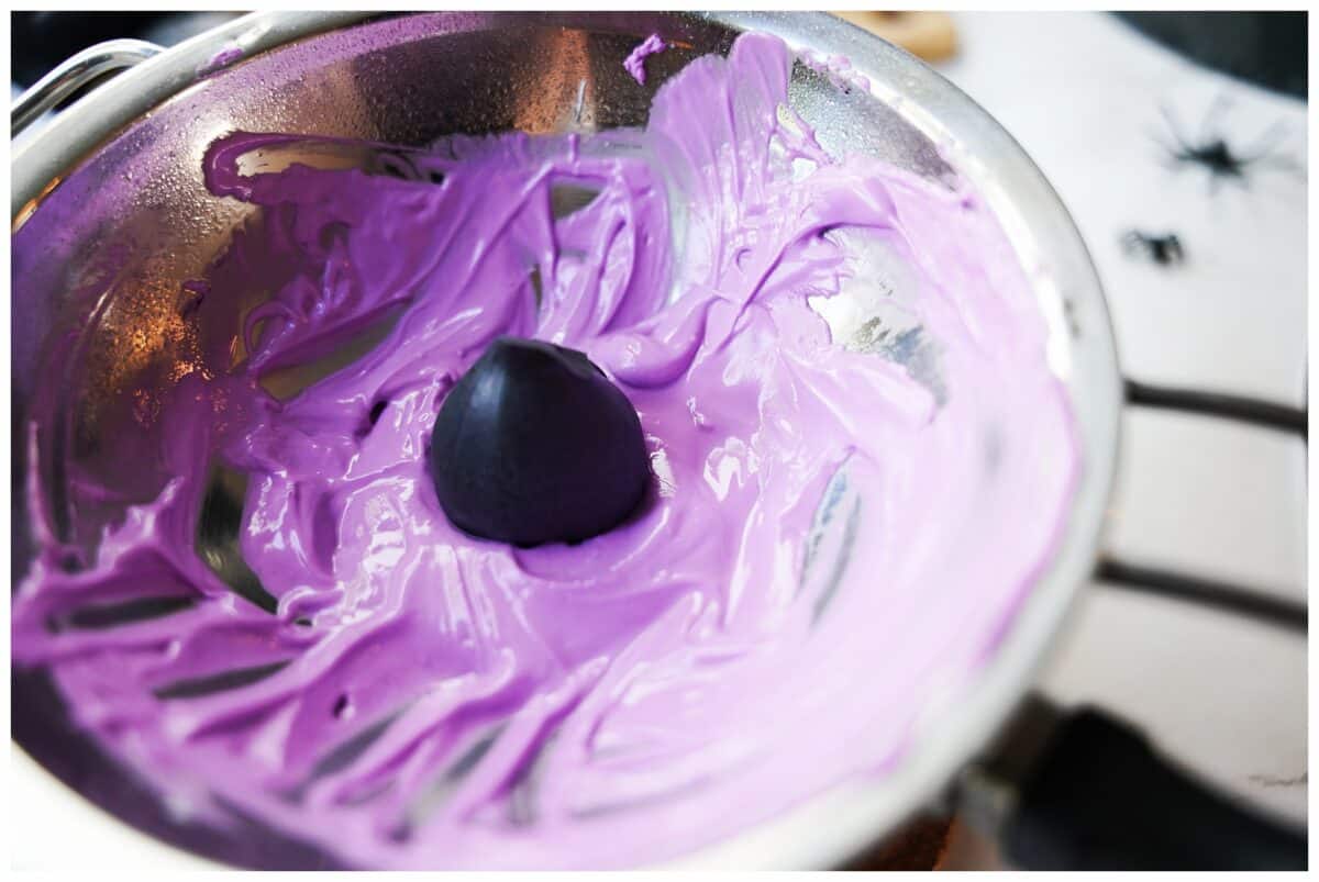 stainless steel bowl with melted purple candy melts dunking a strawberry coated in black candy melts