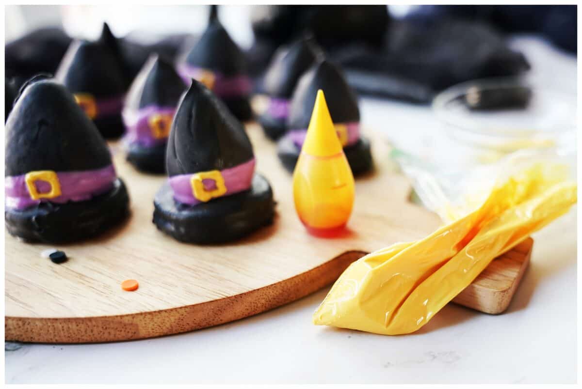 strawberry witch hats on wooden board with bag of yellow icing to pipe on buckle of witch hat