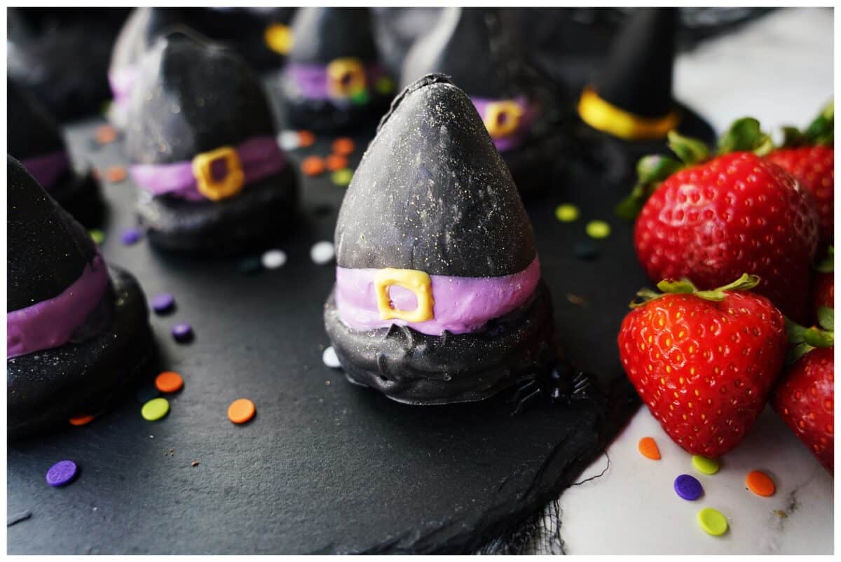 horizontal image of chocolate coated strawberry with black candy melts sitting on top of a Oreo to create a witch hat