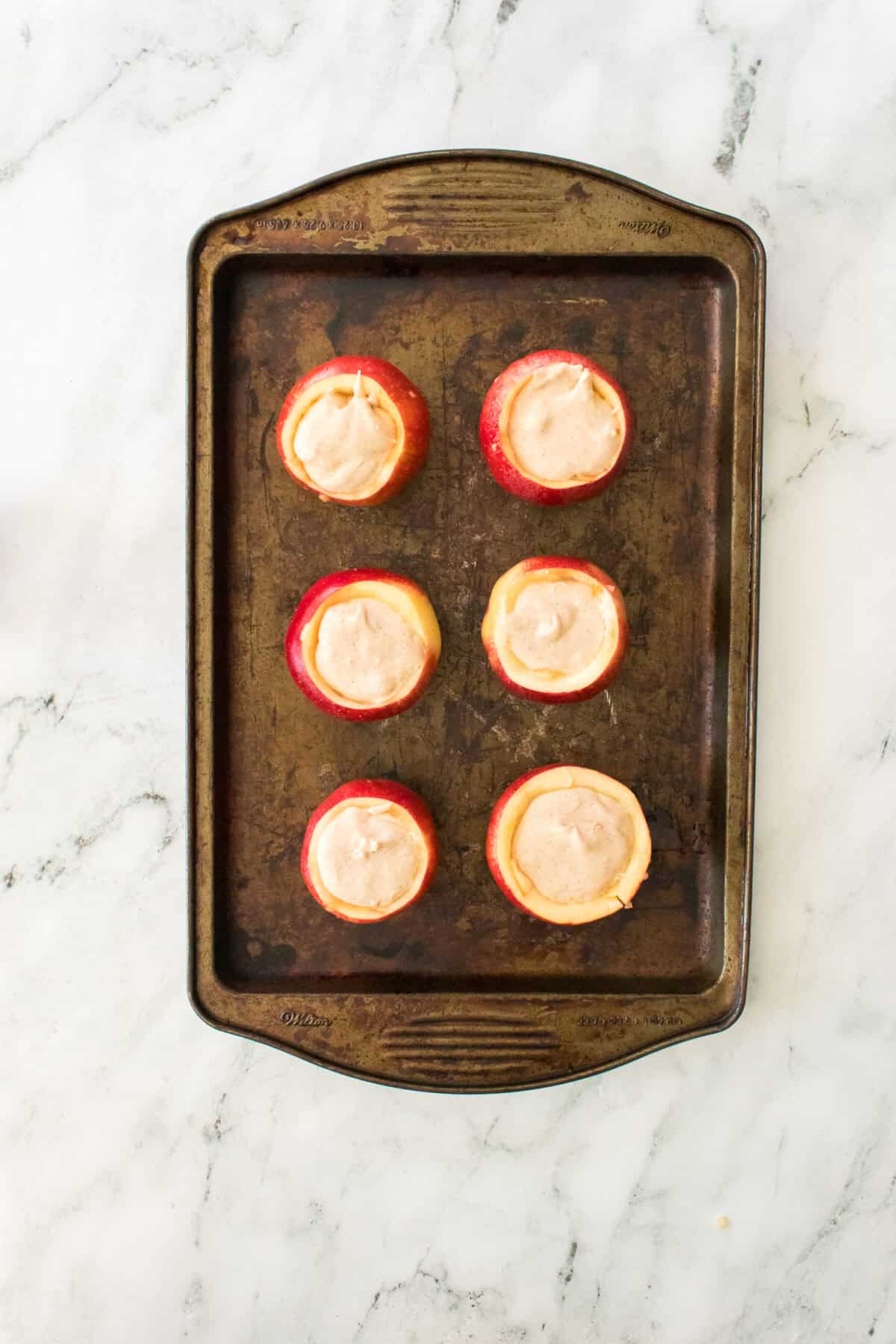 red gala apples with cheesecake filling on baking sheet prior to baking